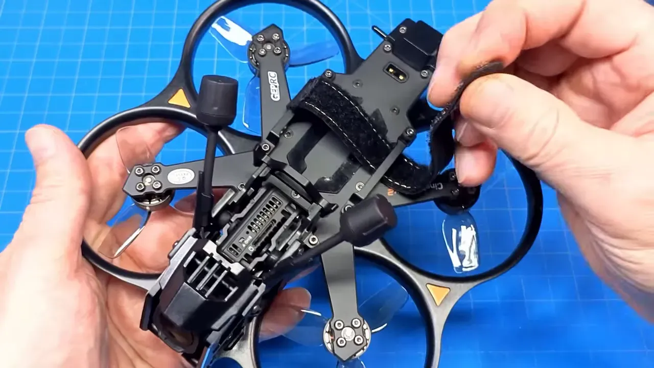 Hands adjusting the GEPRC velcro strap on the Cinebot25 V2 top plate and camera module