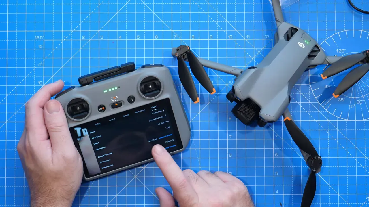 DJI RC on a blue work mat showing the Fly app settings screen; a finger points at the display and a DJI Mini-series drone sits to the right.