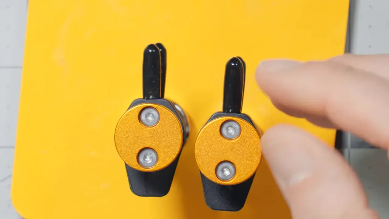 Top-down close-up of two orange circular clip heads on a yellow magnetic base with a finger nearby, showing the fixed-angle compact clips