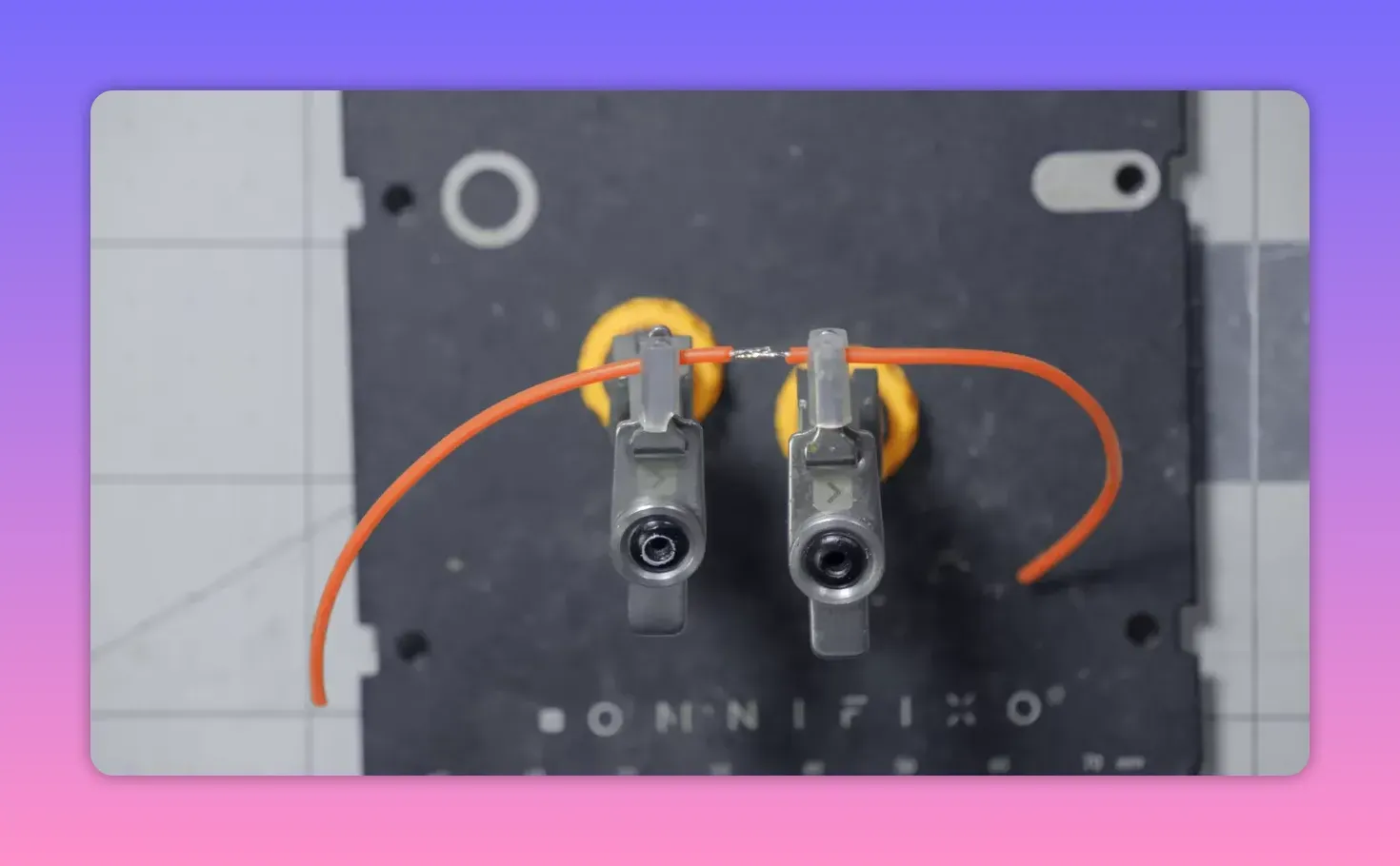 Overhead shot of two metal clips mounted on a black magnetic base holding orange wires aligned with a small tinned splice between them
