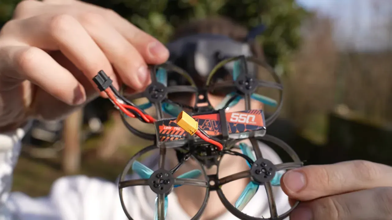 Hand‑held Mobula 8 tiny whoop with visible 550mAh battery pack and connector