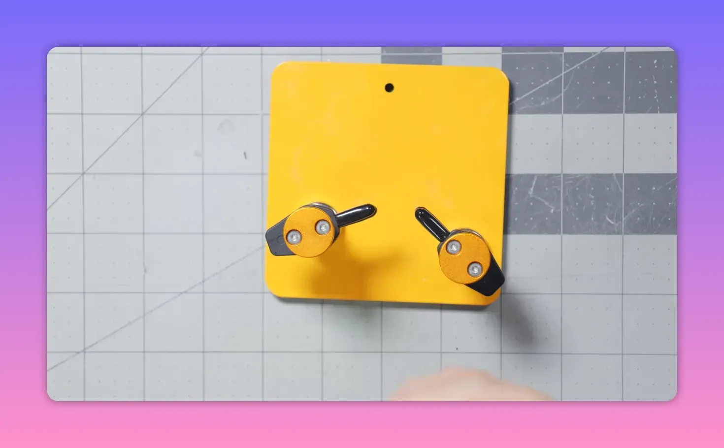 Overhead shot of a yellow magnetic base with two fixed-angle spring clips mounted, placed on a gridded cutting mat