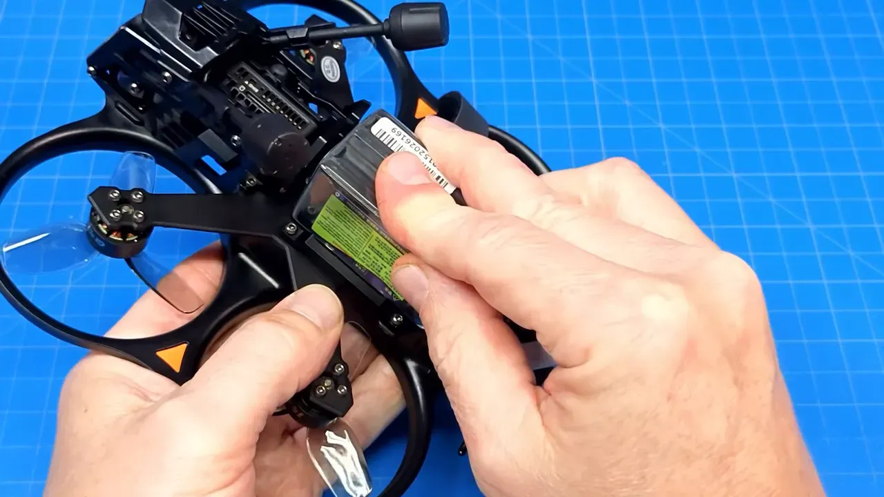 Hands pressing a battery into the Cinebot25 V2 sticky top battery pad with strap