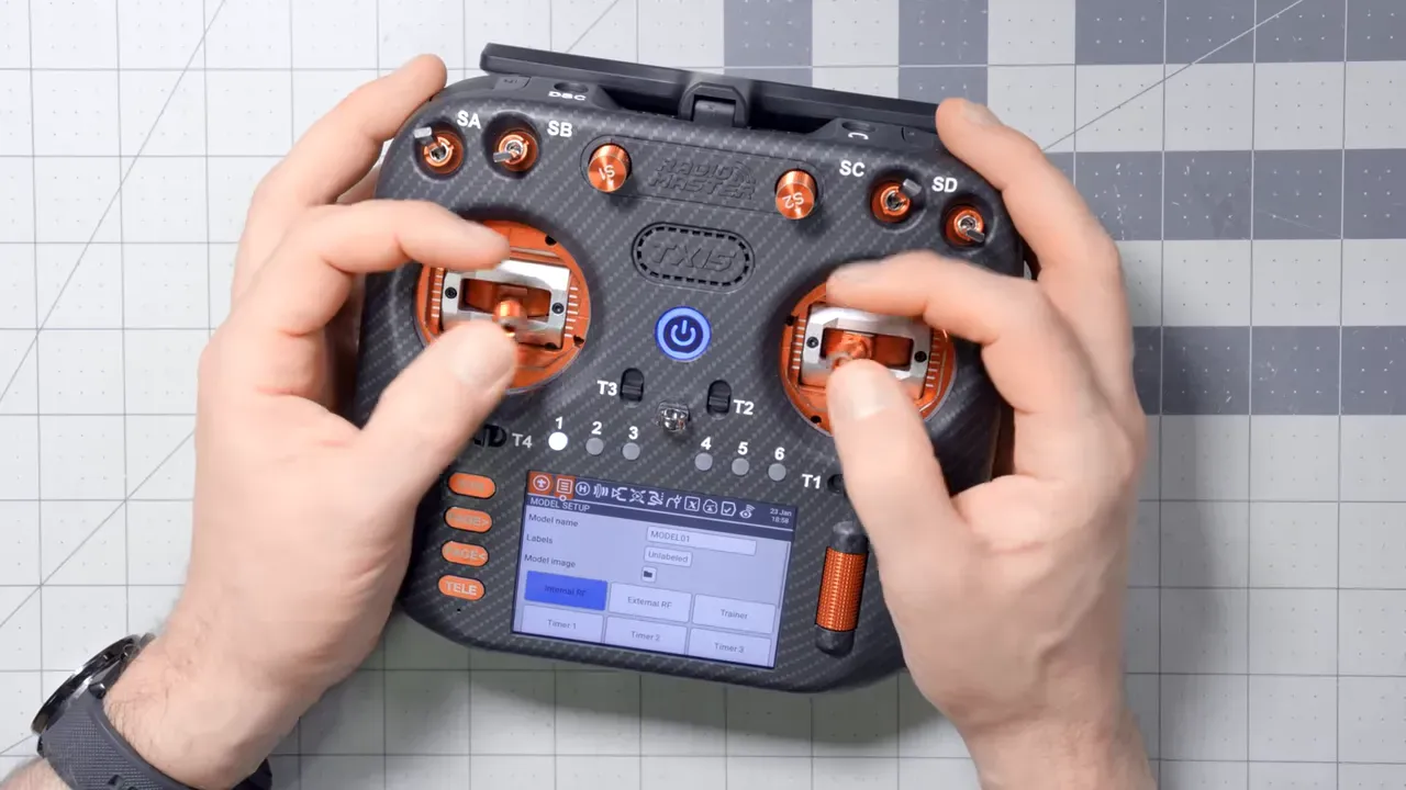 Top-down close-up of a RadioMaster transmitter showing orange metal gimbals, switches and touchscreen with hands resting on the sticks