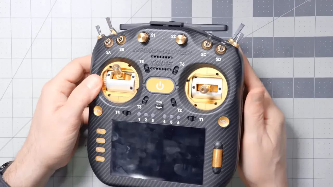 Top-down close-up of a full-size Radiomaster-style transmitter with carbon-fiber finish, gold gimbals, multiple switches and a touchscreen