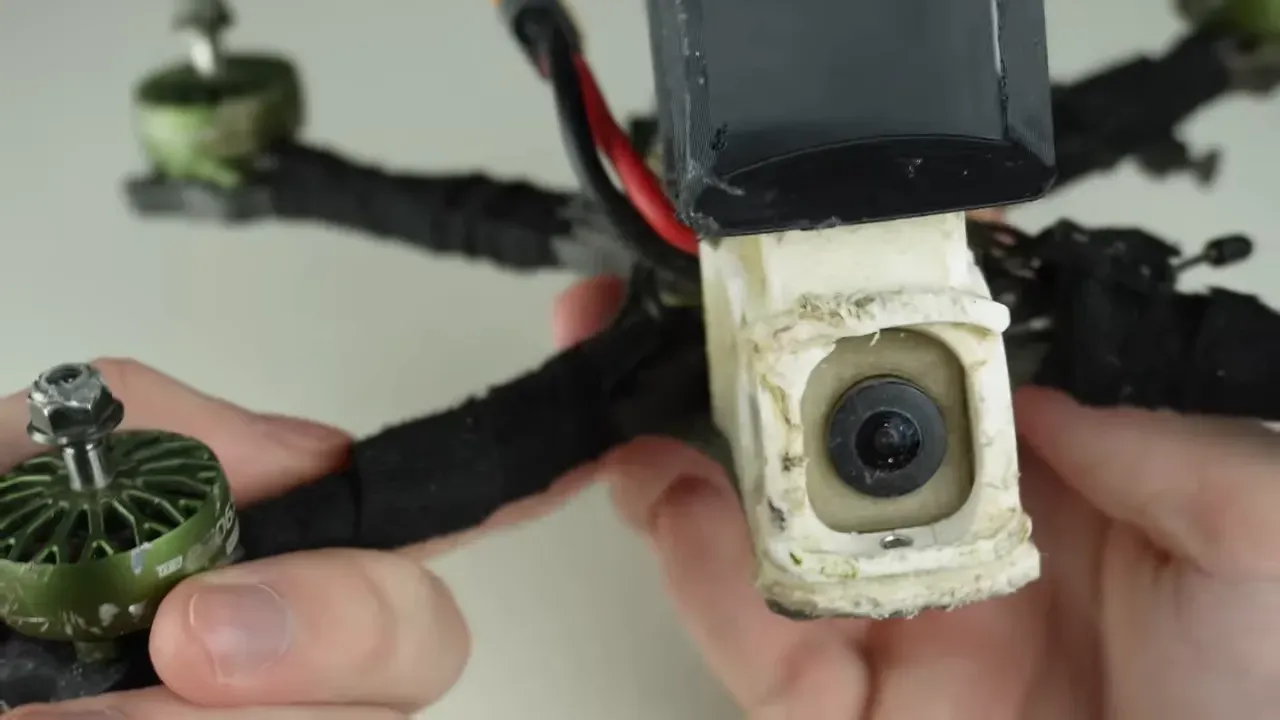 Front-facing close-up of FPV camera and adjacent motor on a beaten but intact quad