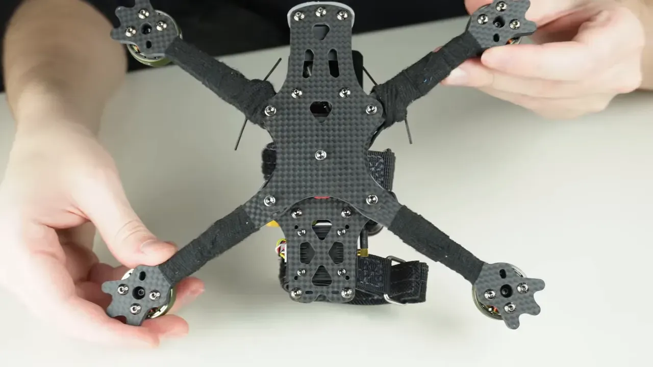 Bottom view of an FPV quad showing carbon fibre arms, screws and antenna wires routed beside the frame