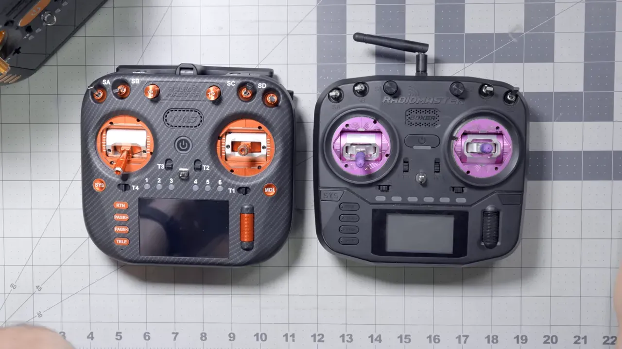 Top-down view of two RadioMaster transmitters on a grid mat — carbon-fiber style TX15 with orange gimbals at left and Boxer with purple gimbals at right.