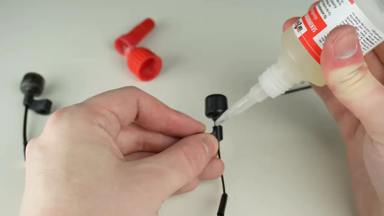 Hands applying glue to an FPV antenna component and cap on a work surface
