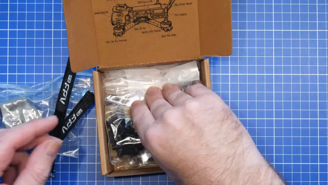 Hands reaching into an FpV ERA Mini kit box showing packaged hardware on a cutting mat