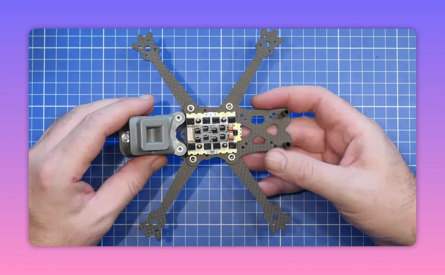 ERA Mini frame with flight controller stack mounted side-on by hands on a blue cutting mat