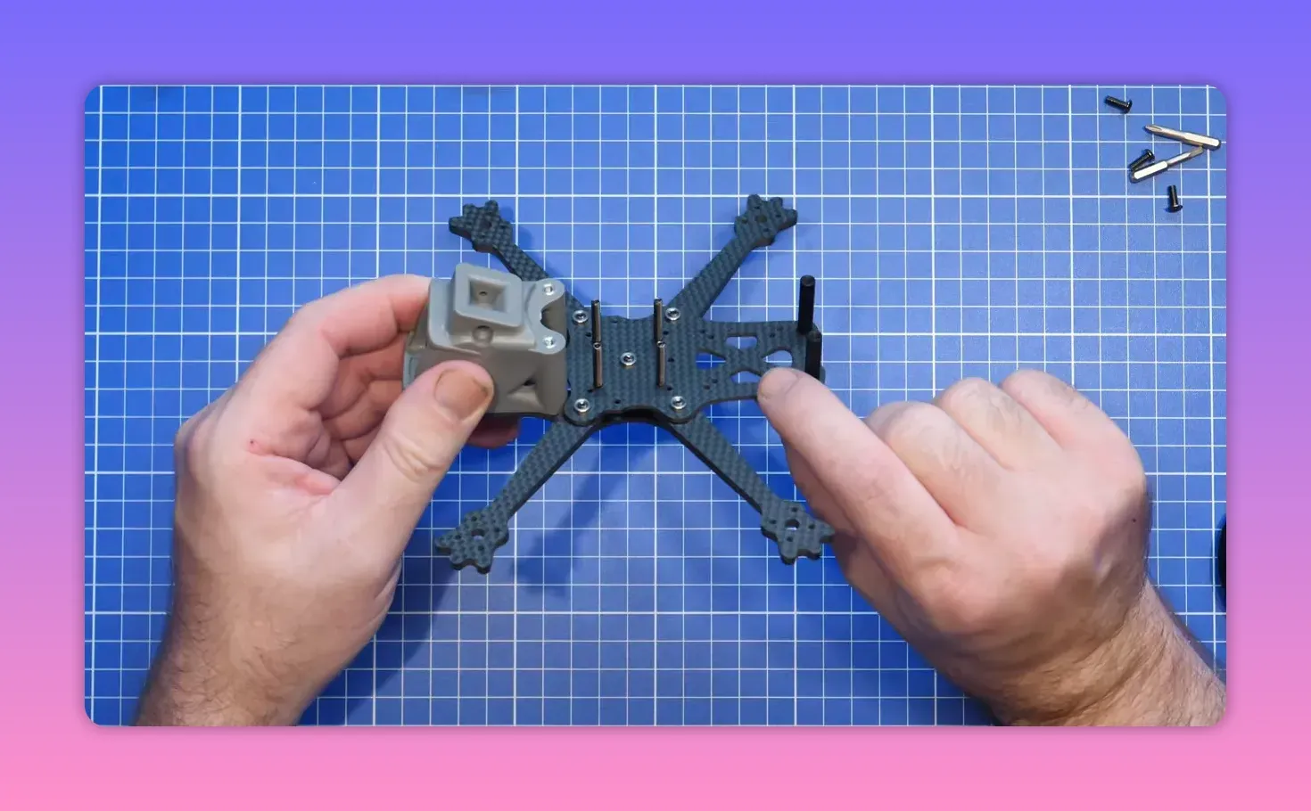 Hands holding an FpV ERA Mini frame during pre-fit assembly on a blue cutting mat