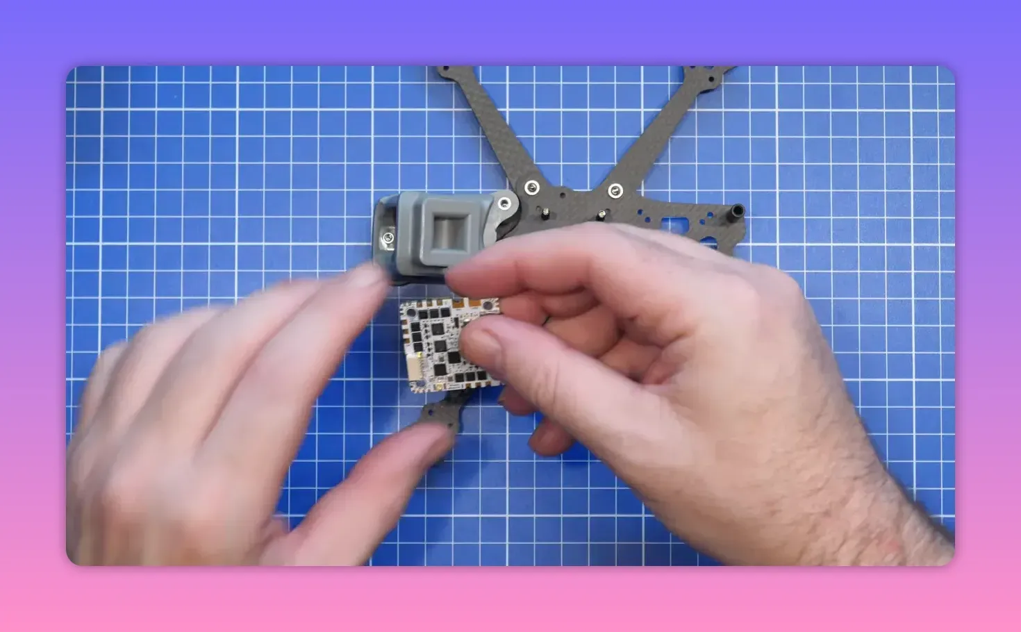 Hands installing the flight controller stack onto the FpV ERA Mini frame on a blue cutting mat