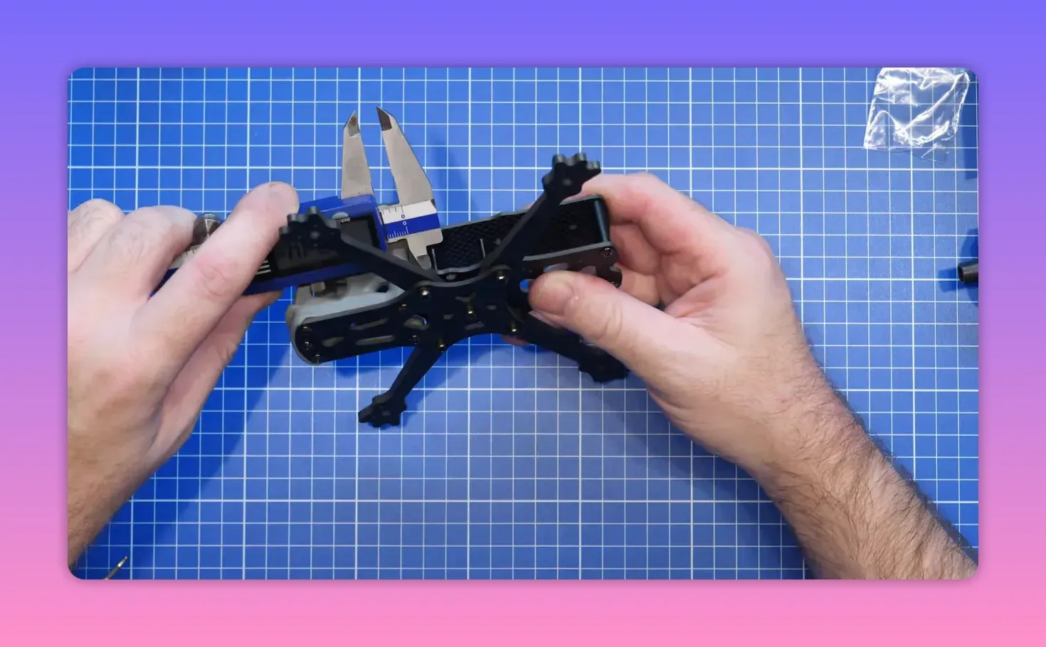 Hands holding and positioning the FpV ERA Mini frame and front camera area on a blue cutting mat