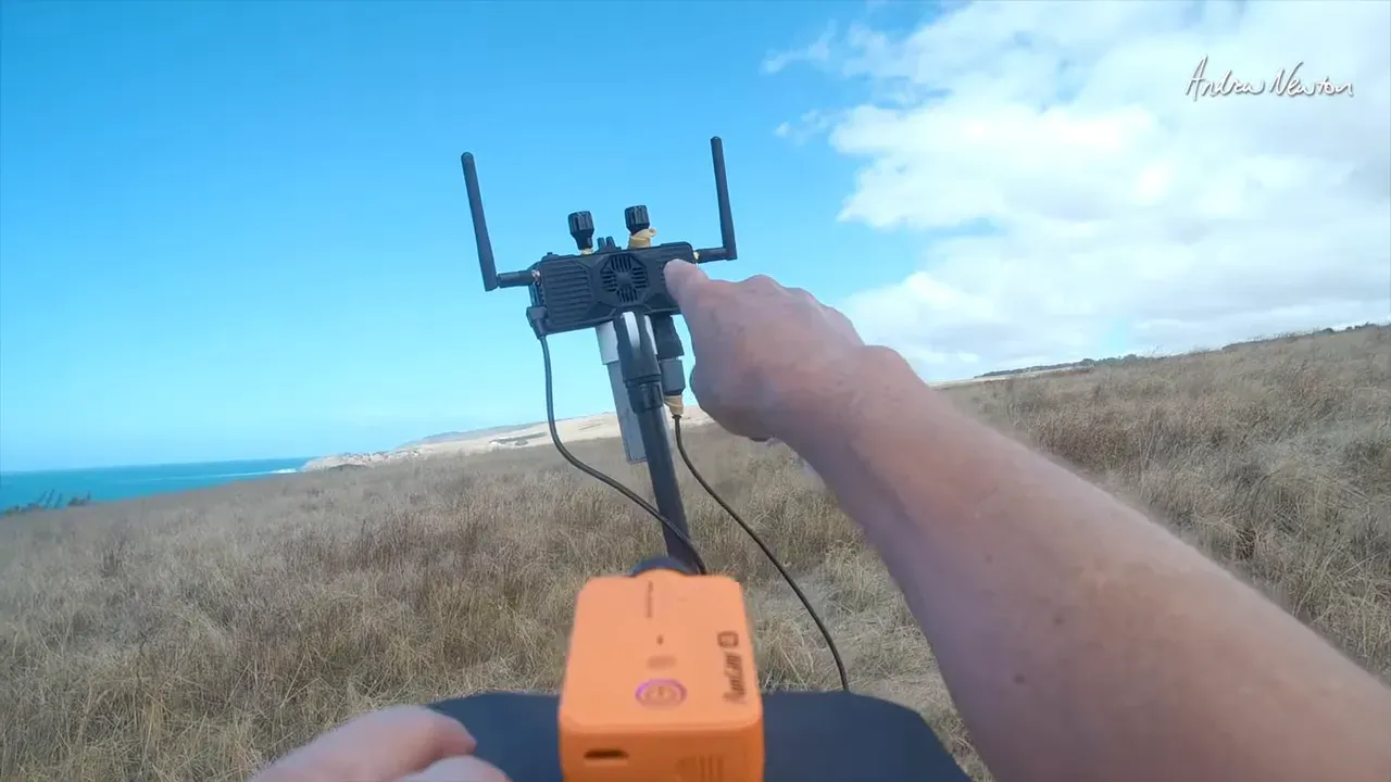Person holding a controller while an external FPV/HDMI-style video module is mounted on a pole outdoors