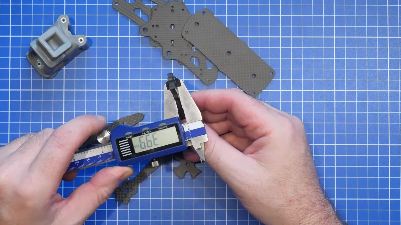 Hands using calipers to measure the ERA Mini frame stack components on a blue cutting mat