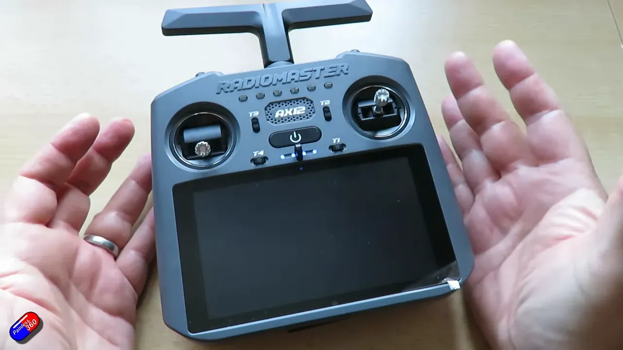 Top-down hands-on view of the RadioMaster AX12 showing the large touchscreen, gimbals and front controls between the user's hands
