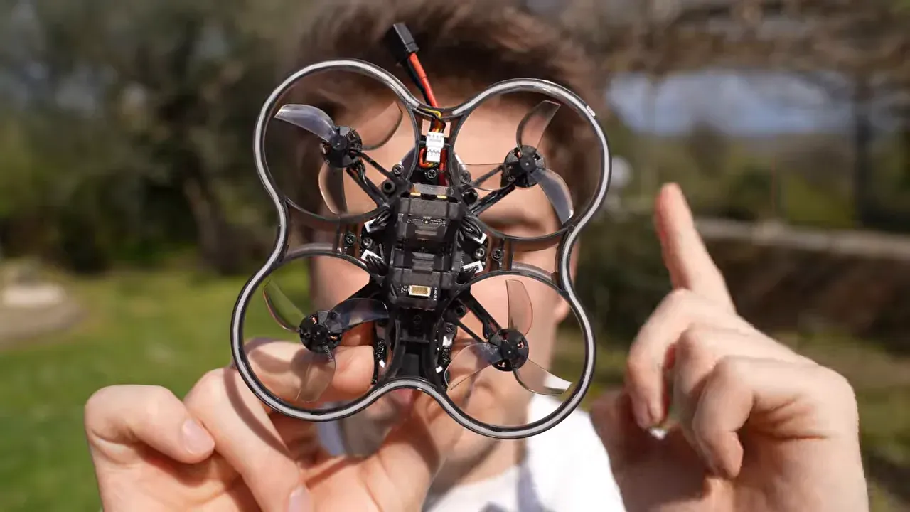 Oxbot Lumo18 tinywhoop held outdoors with electronics visible while indicating SPDB Bluetooth tuning