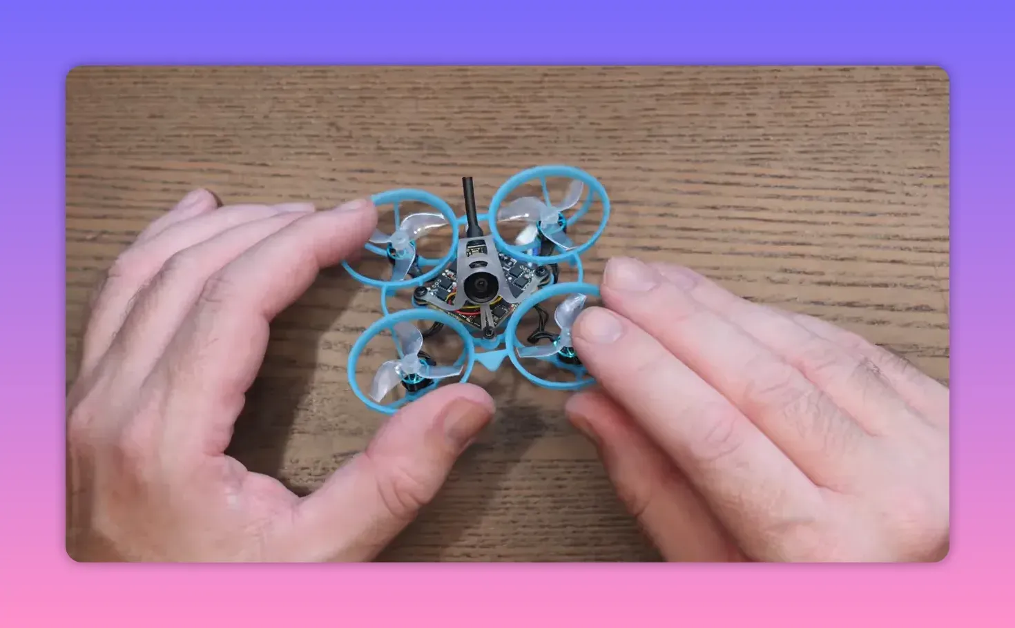 Hands holding the BetaFPV Air65 II Freestyle whoop on a wooden table, showing the frame and onboard electronics