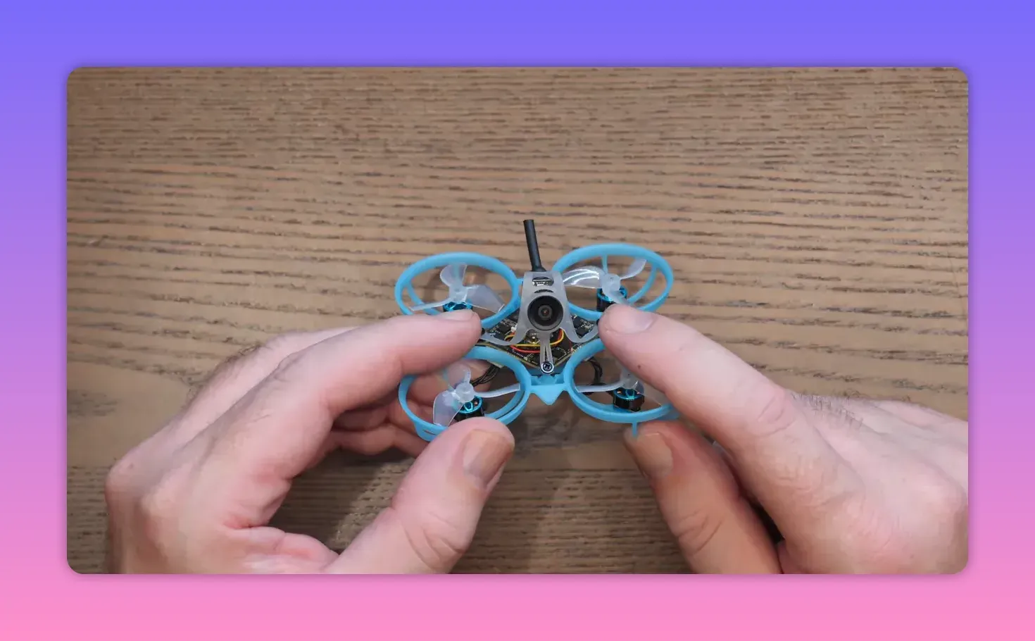Hands holding the BetaFPV Air65 II freestyle whoop with camera and onboard electronics visible on a wooden table