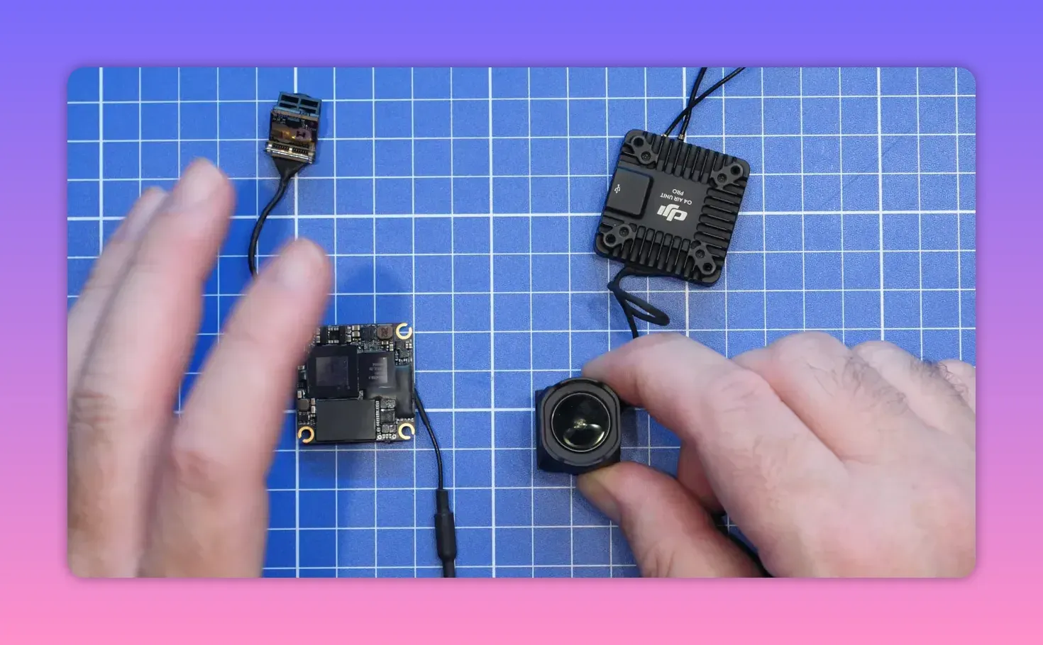 Clear close-up of FPV camera PCB and gyro-related module on a grid workbench with hands and connected parts