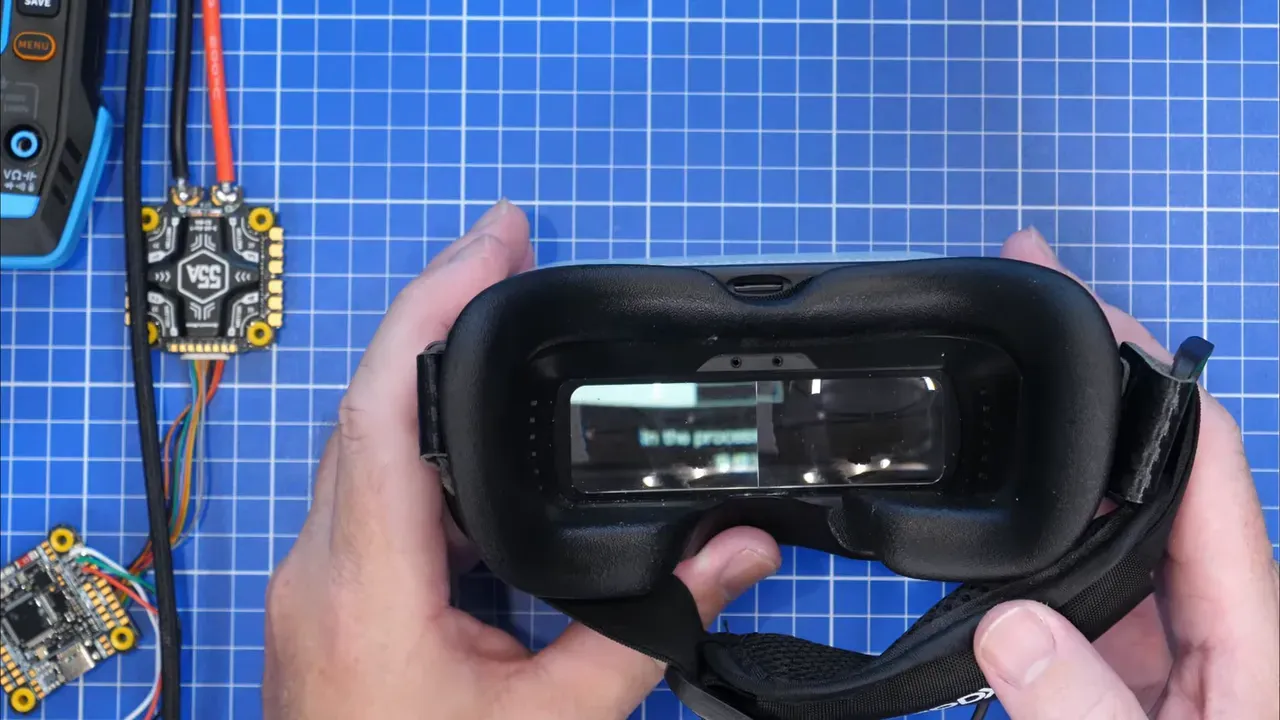 FPV goggles screen showing firmware version menu while being held over a blue cutting mat