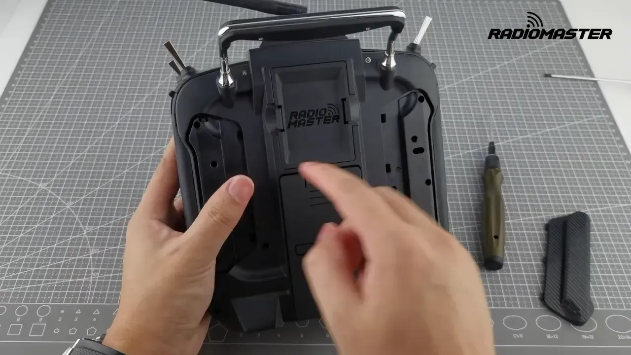 Back of the TX16S showing two access holes behind the left side with a finger indicating one hole