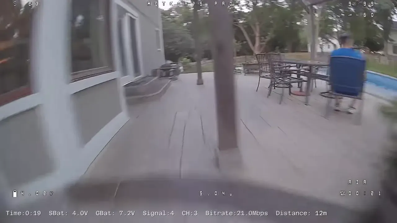 FPV view flying under a covered patio with chairs and columns visible
