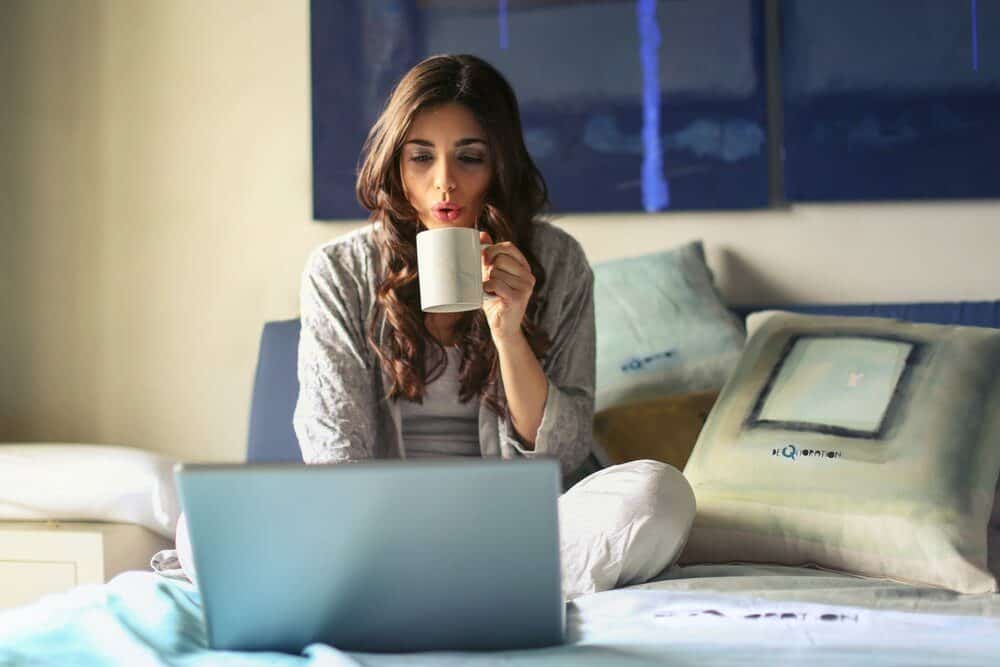 woman-in-grey-jacket-sits-on-bed-uses-grey-laptop-935743-3365753